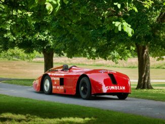 Restored red Sunbeam 1000hp land-speed car parked beneath trees at Beaulieu, seen from the rear quarter