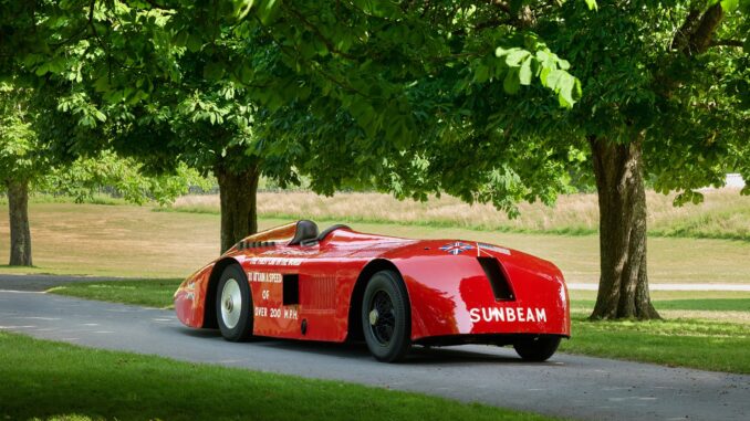 Restored red Sunbeam 1000hp land-speed car parked beneath trees at Beaulieu, seen from the rear quarter