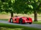 Restored red Sunbeam 1000hp land-speed car parked beneath trees at Beaulieu, seen from the rear quarter
