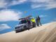 MINI's Rebelle Rally team beside a camouflaged MINI SUV on a sand dune during training.