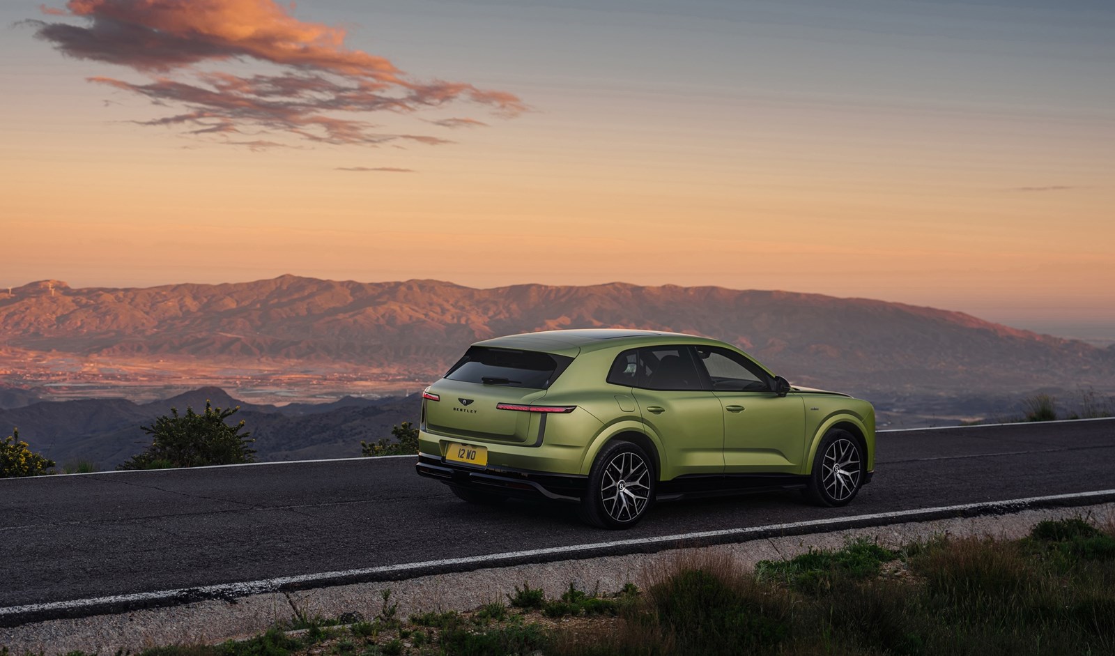 Rear three-quarter view of the all-new Bentley Torcal in light green on a mountain road at sunset