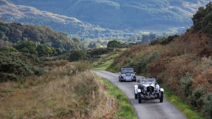 Two pre-war classic cars on a single-track road in the Scottish Highlands