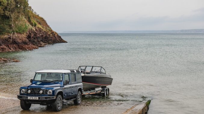 Blue INEOS Grenadier Helmsman recovering a motorboat on a trailer at a coastal slipway