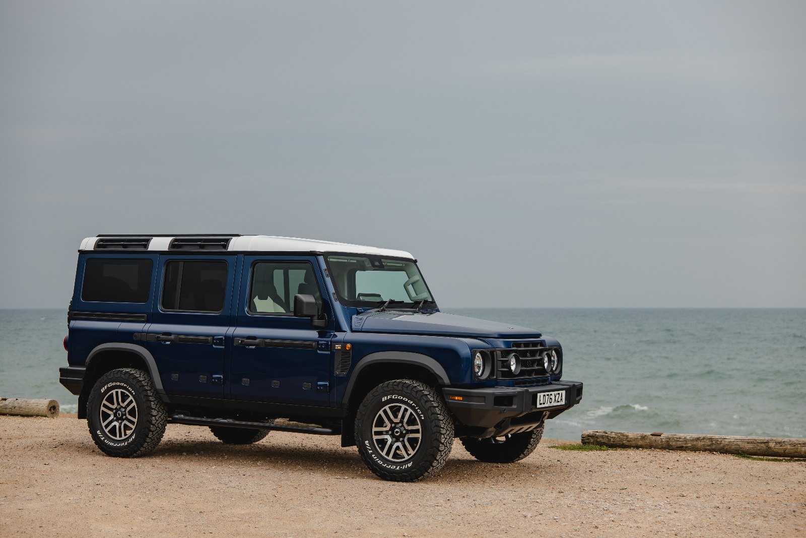Side profile of the INEOS Grenadier Helmsman with white contrast roof and 17-inch diamond-cut alloy wheels on a beach