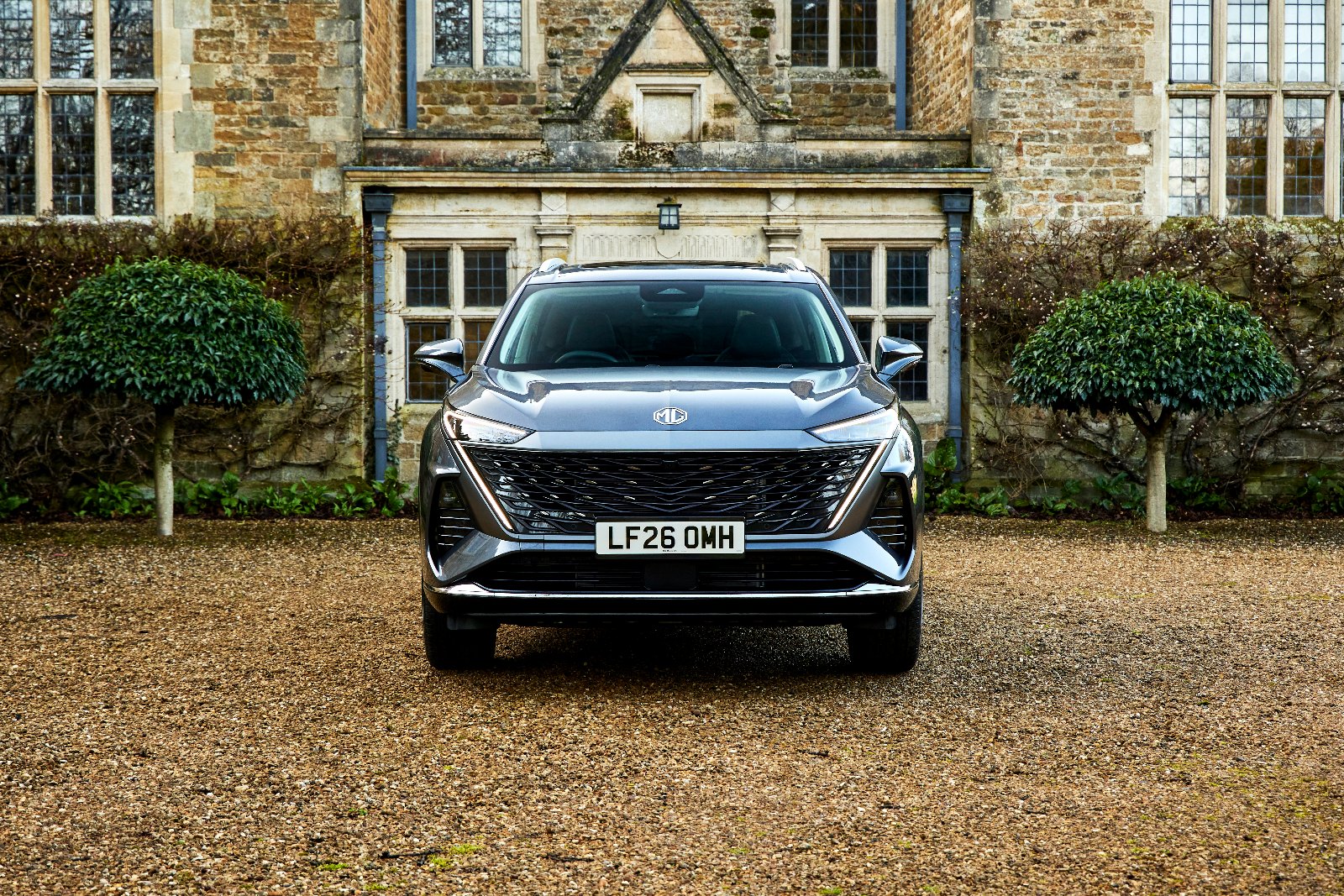 The MG MGS9 PHEV in Camden Grey parked on gravel in front of a stone country house, front view