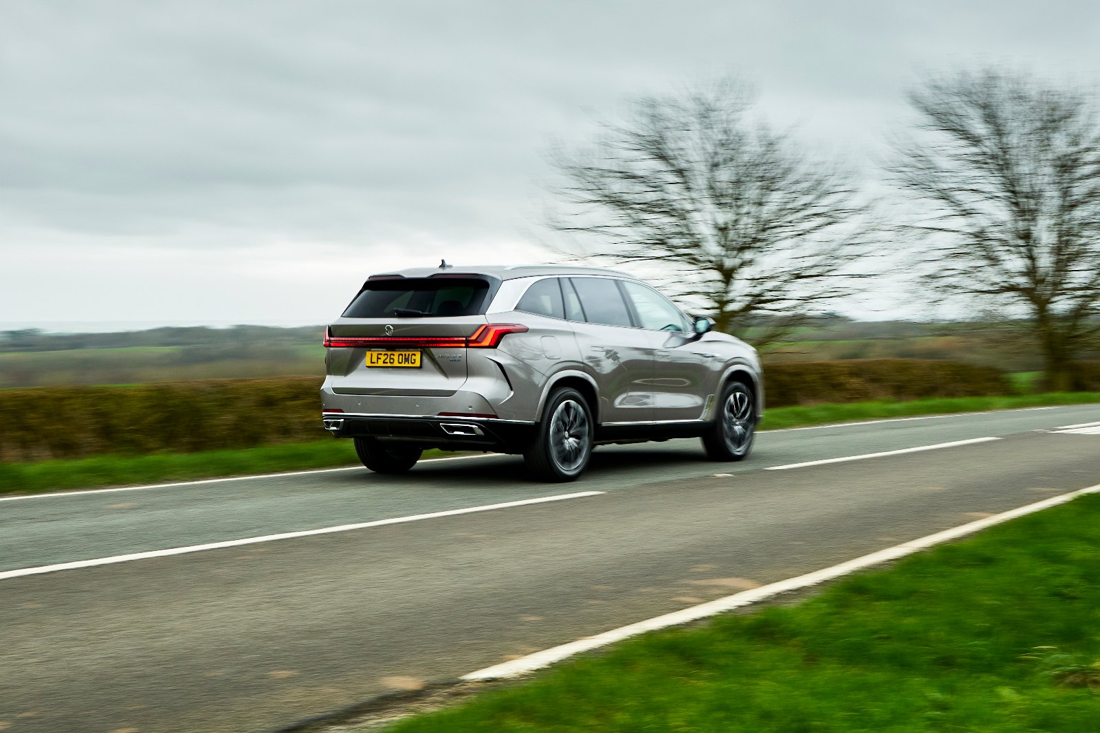 Silver MG MGS9 PHEV driving away on a rural road, rear three-quarter view