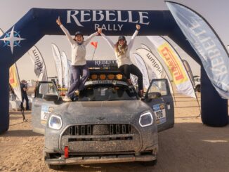 Felicia Killman and Erika Ferrer stand on their dust-covered MINI Countryman celebrating under the Rebelle Rally finish arch