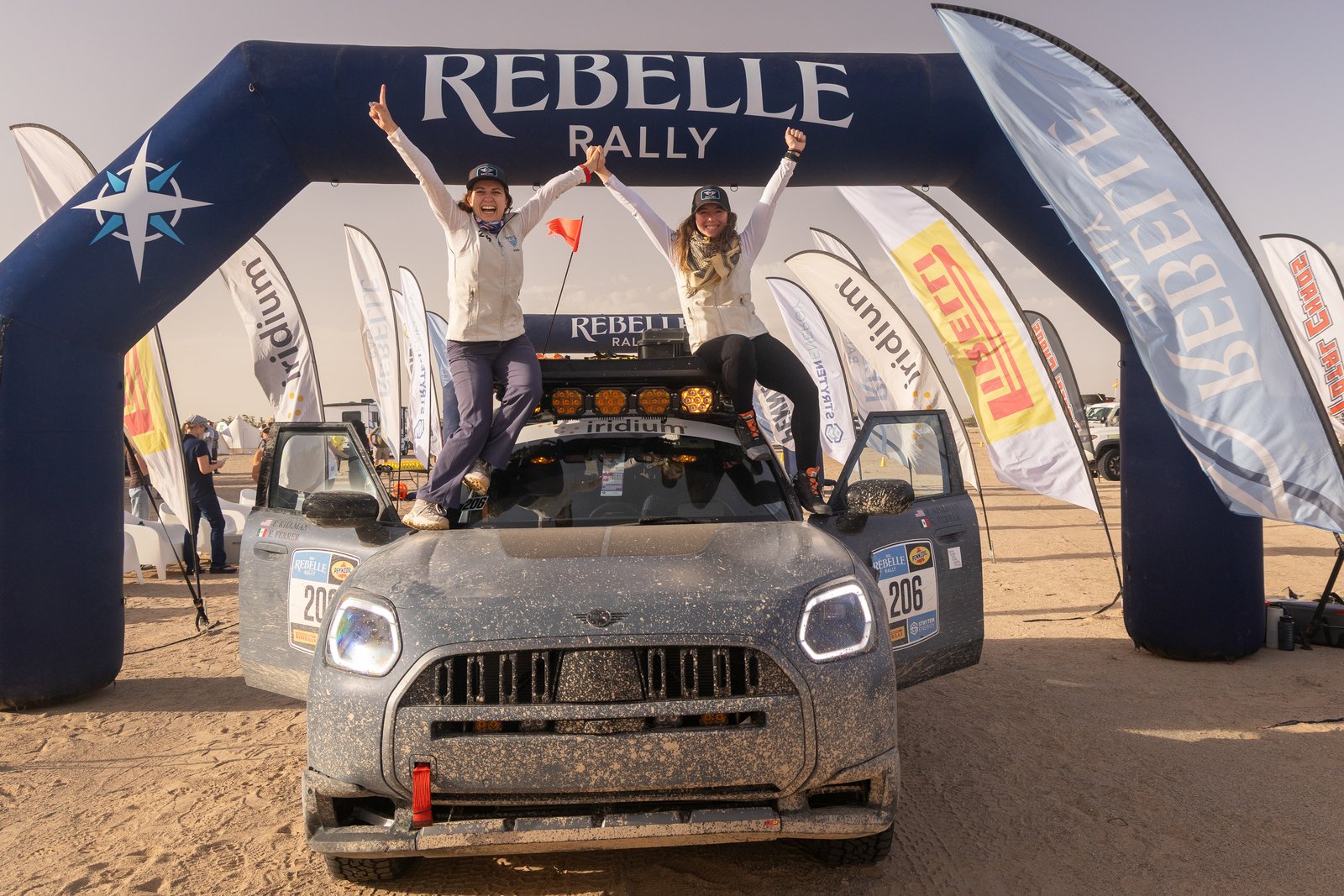 Felicia Killman and Erika Ferrer stand on their dust-covered MINI Countryman celebrating under the Rebelle Rally finish arch